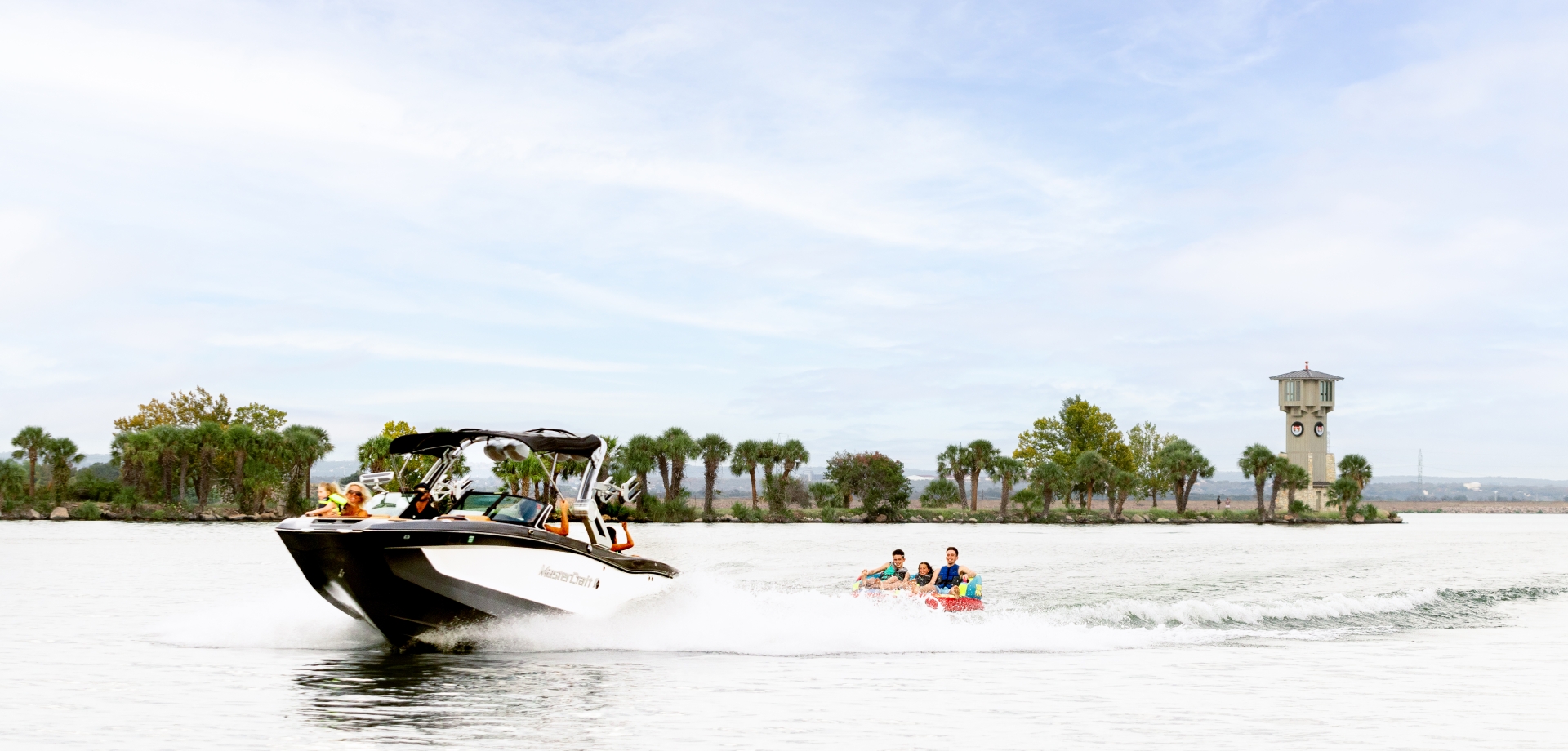 Boat taking kids tubing on lake LBJ, lighthouse in the background on a sunny day.