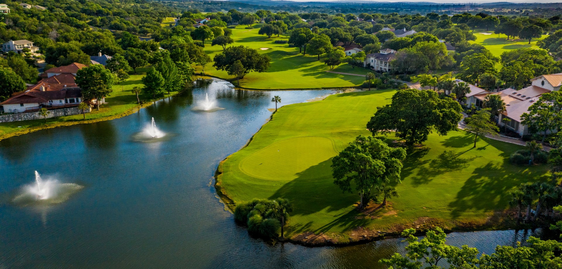 Large body of water with three fountains next to the green of a golf course.